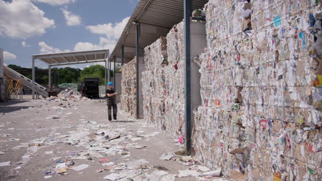 Worker-controls-paper-bales-at-outdoor-recycling-plant,-wide-push-in