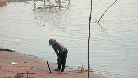 medium exterior shot of man hammering post into the sand with a heavy hammer working on the shore of lake in the daytime