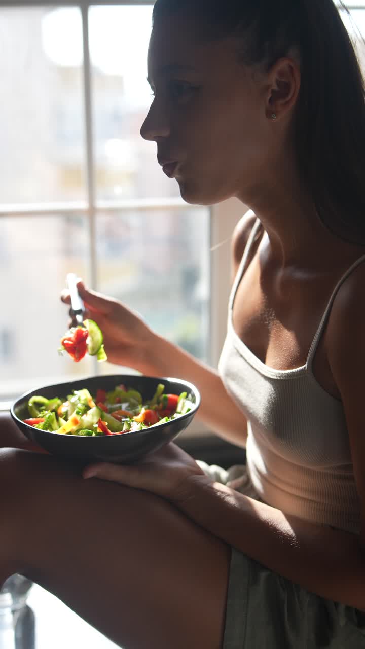 mujer comiendo una ensalada saludable junto a la ventana