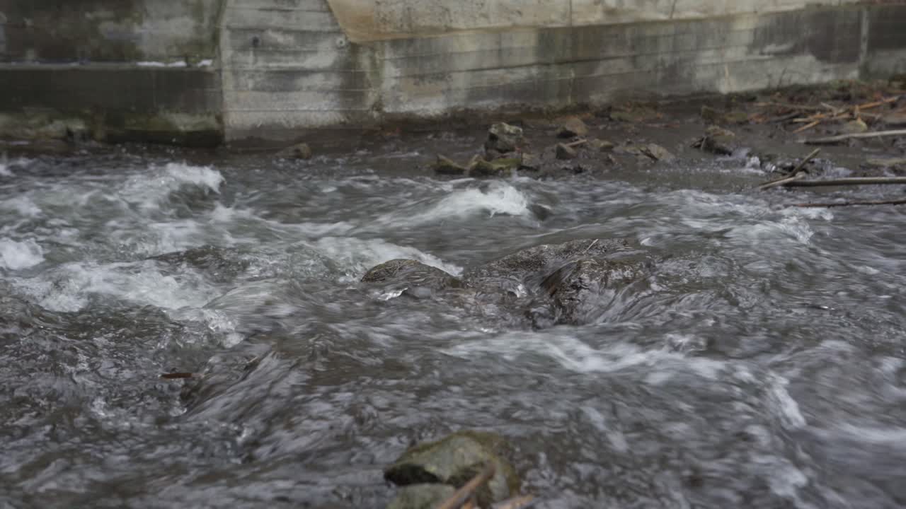 Corriente fluvial rápida fluyendo sobre rocas debajo de una compuerta de hormigón