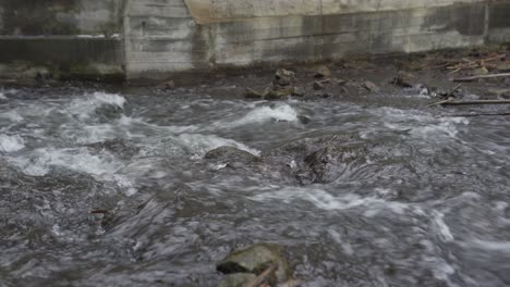Fast river current flowing over rocks below concrete sluice wall