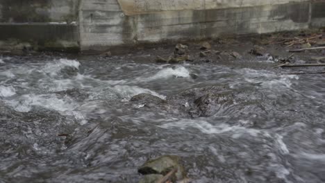 fast river current flowing over rocks below concrete sluice wall