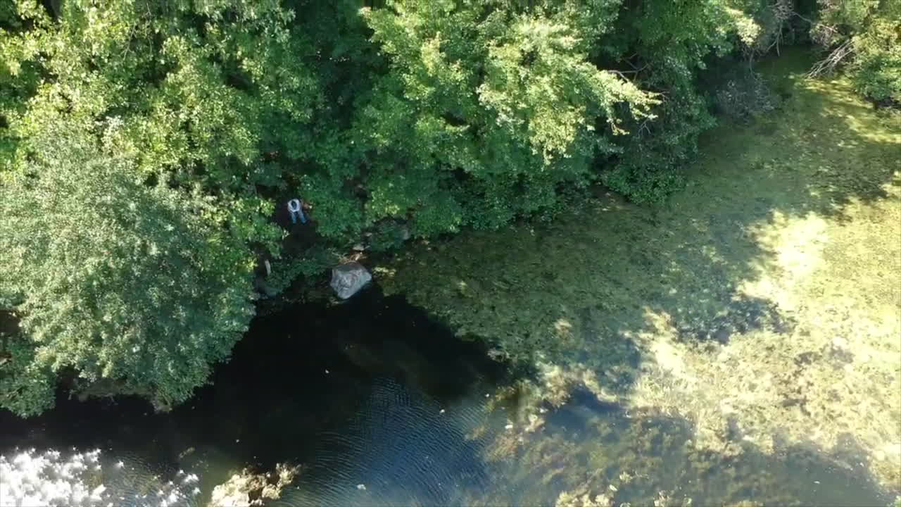 Drone ascending over a pond with a person in the distance