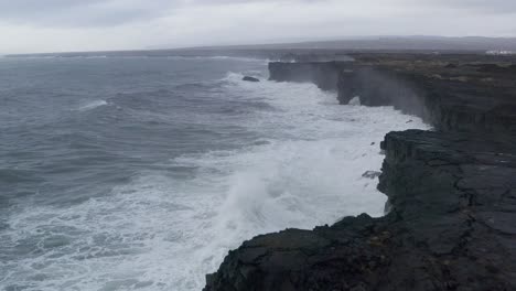 Aerial-flight-along-crashing-waves-of-ocean-at-Coast-near-town-Þorlákshöfn,-Iceland