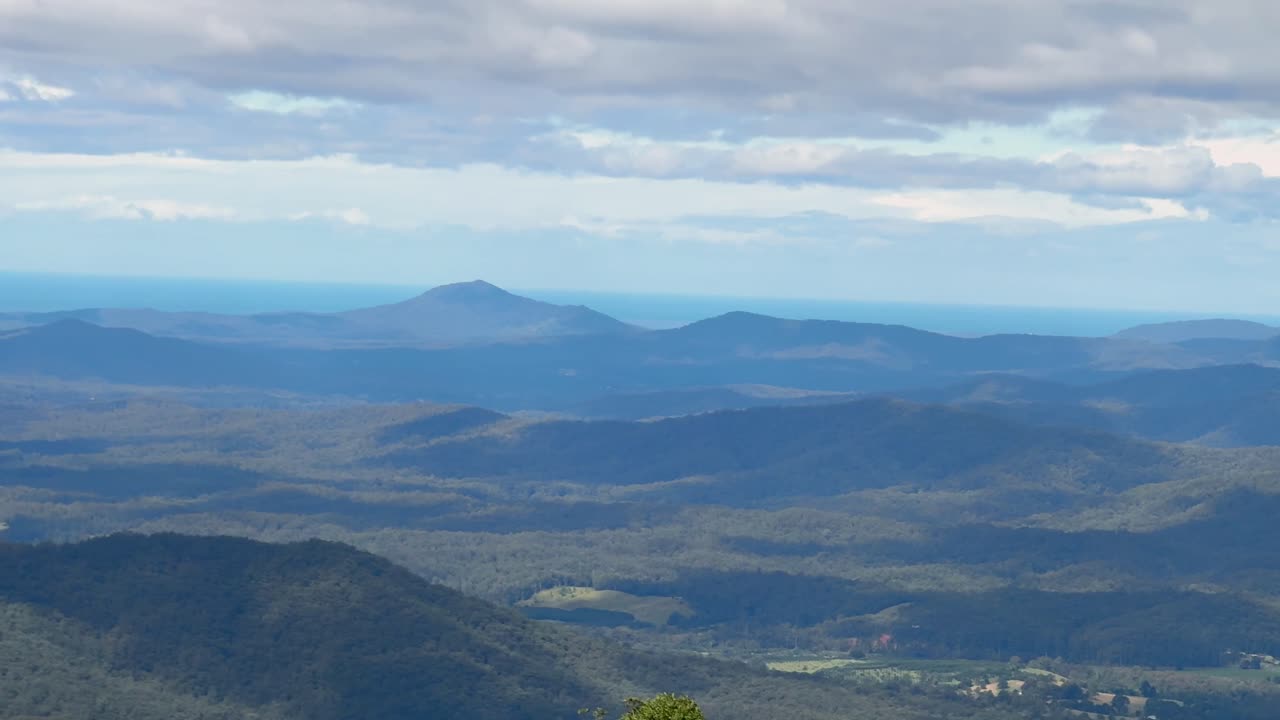 Camera smoothly pans across Dorrigo Mountain in New South Wales, Australia, revealing rolling hills, dense forests, and distant blue ridges under soft daylight