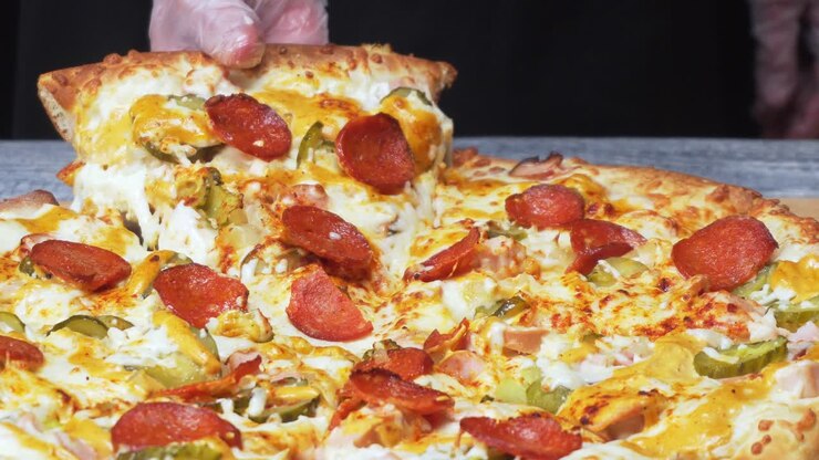 Mano che prende una fetta di pizza con pepperoni, salsiccia e cetriolini