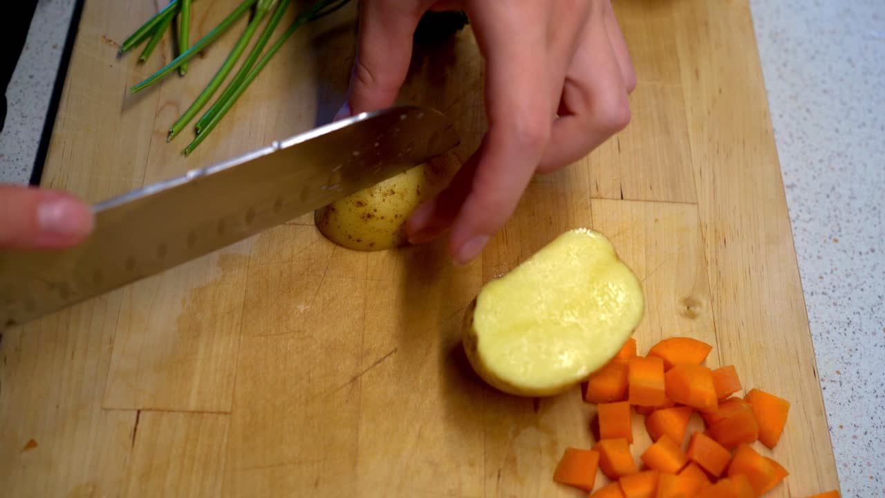 Female Hands Cutting a Potatoes on a Wooden Cutting Board With Parsley and Diced Carrots in the Background