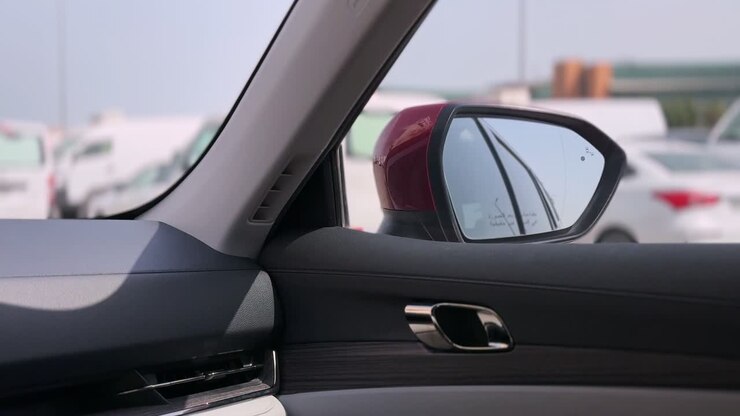 Primo piano di un pannello della portiera di un'auto moderna e dello specchietto laterale con veicoli parcheggiati all'esterno alla luce del giorno, che mostra un design interno pulito e uno sfondo urbano sfocato e morbido