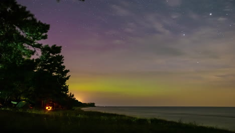 Aurora-Borealis-Visible-En-El-Cielo-Nocturno-Estrellado-Con-Campistas-Y-Carpa-En-La-Orilla