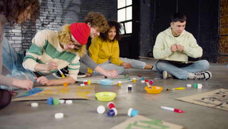 jóvenes activistas ambientales pintando carteles sentados en el suelo