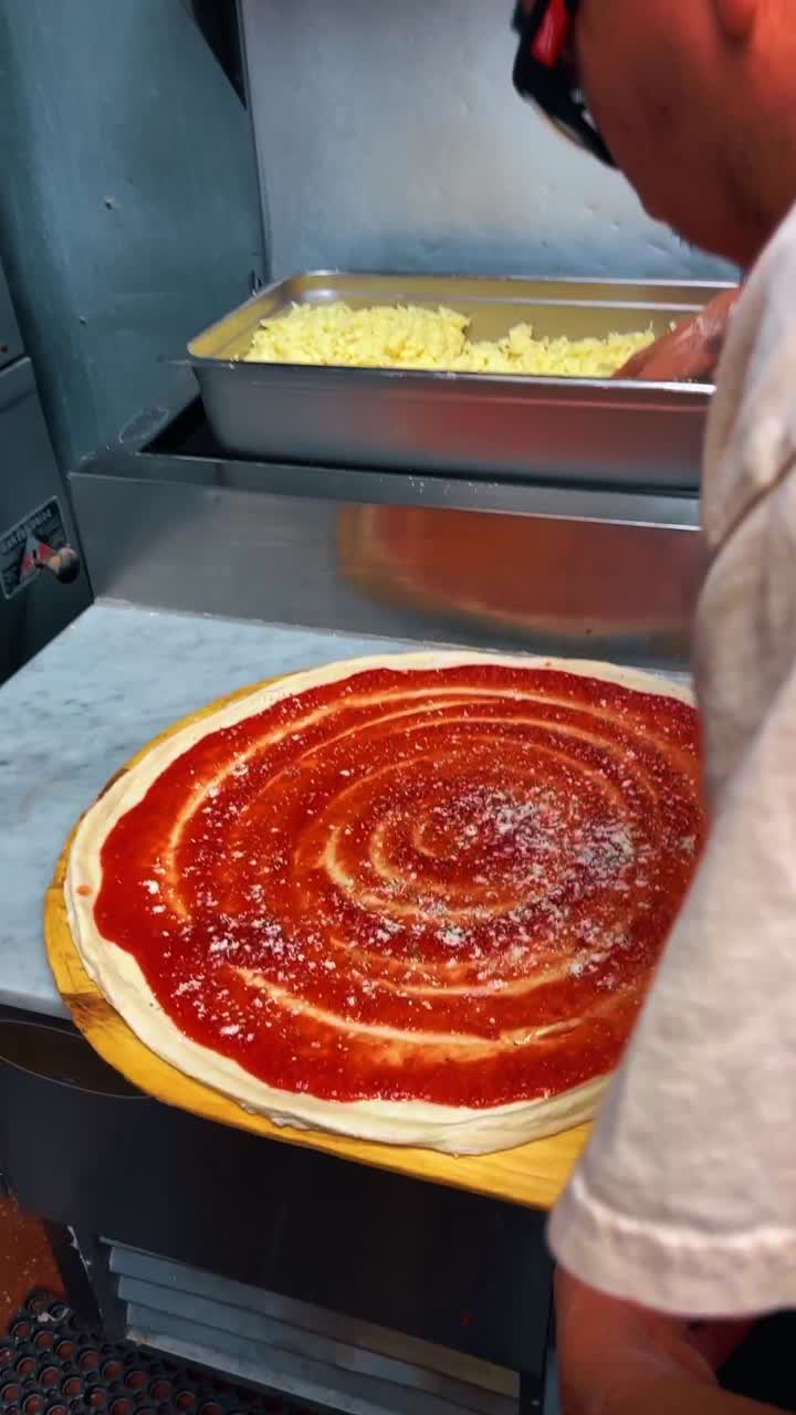 Cospargere formaggio grattugiato sulla salsa per pizza su impasto crudo. Primo piano in azione di una mano che aggiunge formaggio bianco su una base di pomodoro rossa durante la preparazione della pizza.