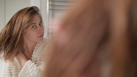 brunette lady enjoys reflection in mirror after undergoing beauty treatment in shower. attractive female admires silky hair looking in mirror slow motion