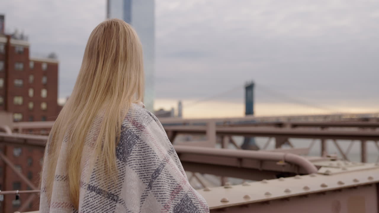 Young woman wrapped in blanket on Brooklyn Bridge with Manhattan skyline in New York