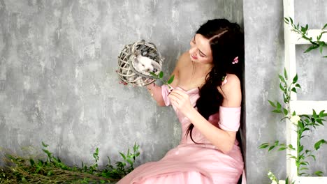 young lady posing in photo studio holding small white rabbit in wicker grey basket, girl having fun