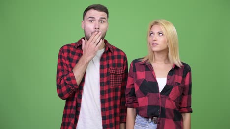 Young man covering mouth while looking guilty with young woman