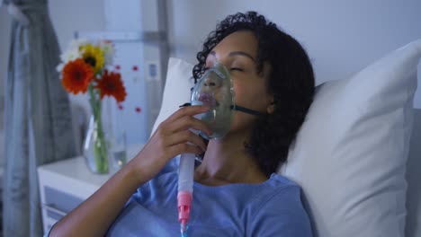 portrait of african american female patient lying on hospital bed wearing oxygen mask ventilator