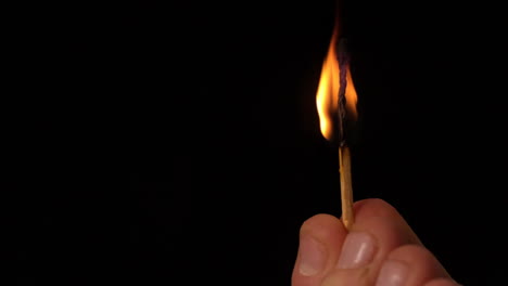 Hand-holding-match-burning-out-on-black-background