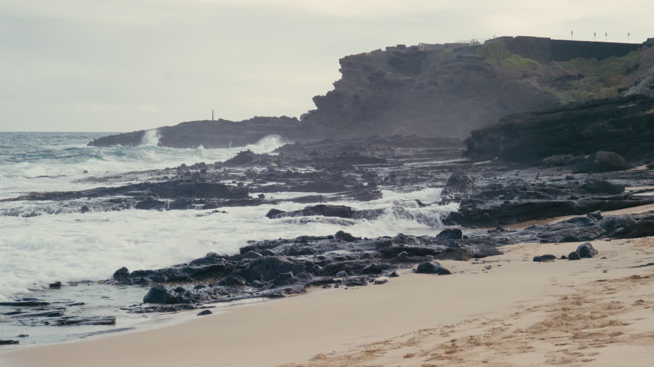 Sandy beach landscape with waves splashing on rocks and cliffside in the background