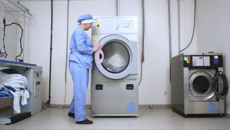 Female-worker-loading-washing-machine-at-hotel-laundry.-Commercial-laundry-room