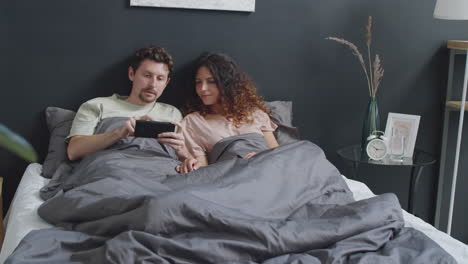 couple watching something on a smartphone in bed