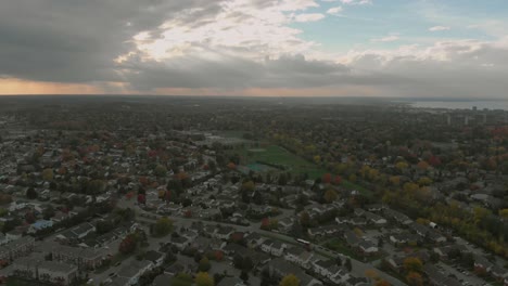 aerial footage above a small town outside a larger city with a large river and sky scrapers in the distance with a huge sunset in the sky