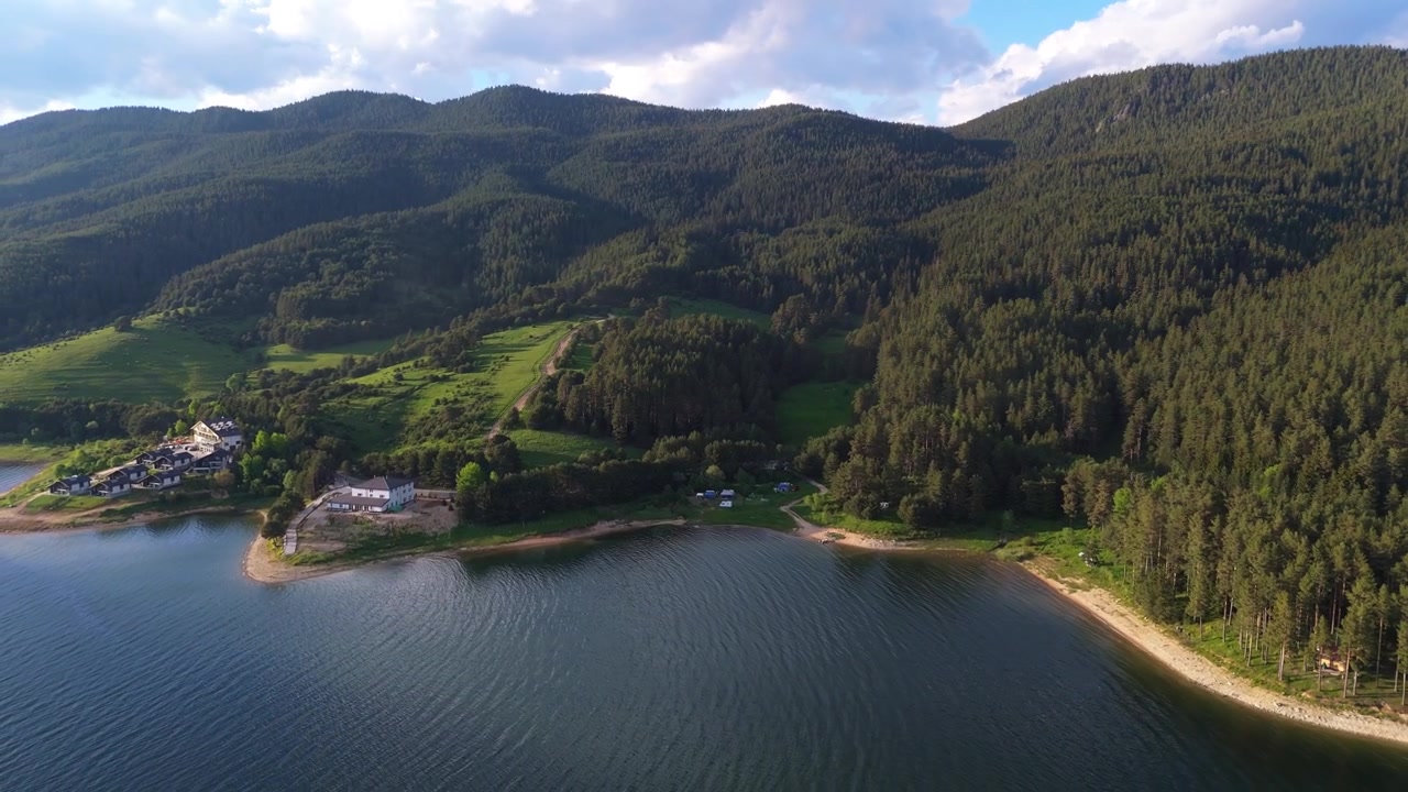 Ripresa panoramica con drone sull'acqua della superficie calma del lago che avvolge la costa boscosa e le montagne presso il bacino di Dospat nella regione dei Rodopi, Bulgaria