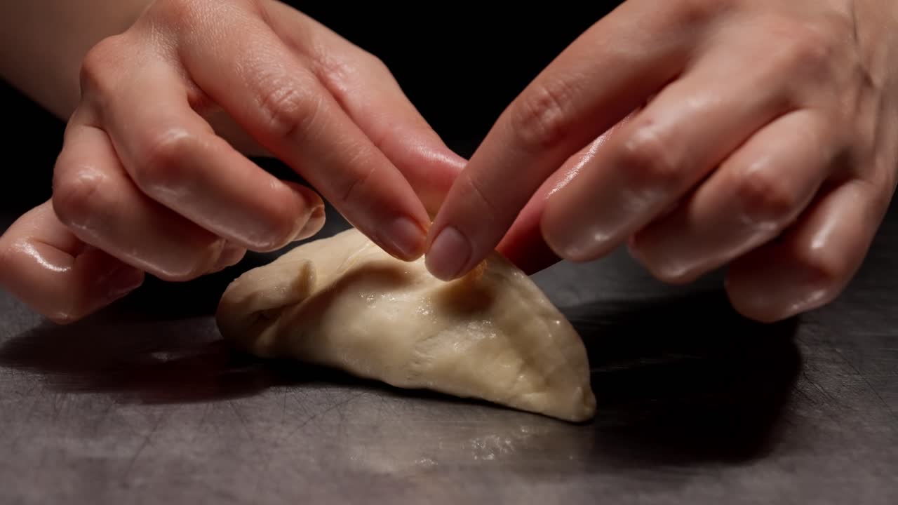 Primo piano di mani che modellano impasto crudo su una superficie metallica