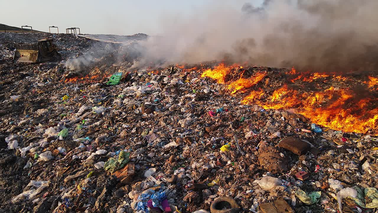 Flames raging across trash mound at landfill site in panning video