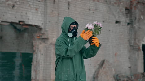 woman ecologist in safety suit holding dying flowers. human wearing gas mask and hazmat costume in abandoned building. environmental problems in polluted zone.