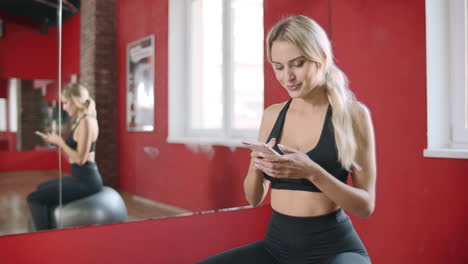 Hermosa-Mujer-Usando-Un-Teléfono-Inteligente-En-El-Gimnasio.-Mujer-Sonriente-En-Forma-Descansando