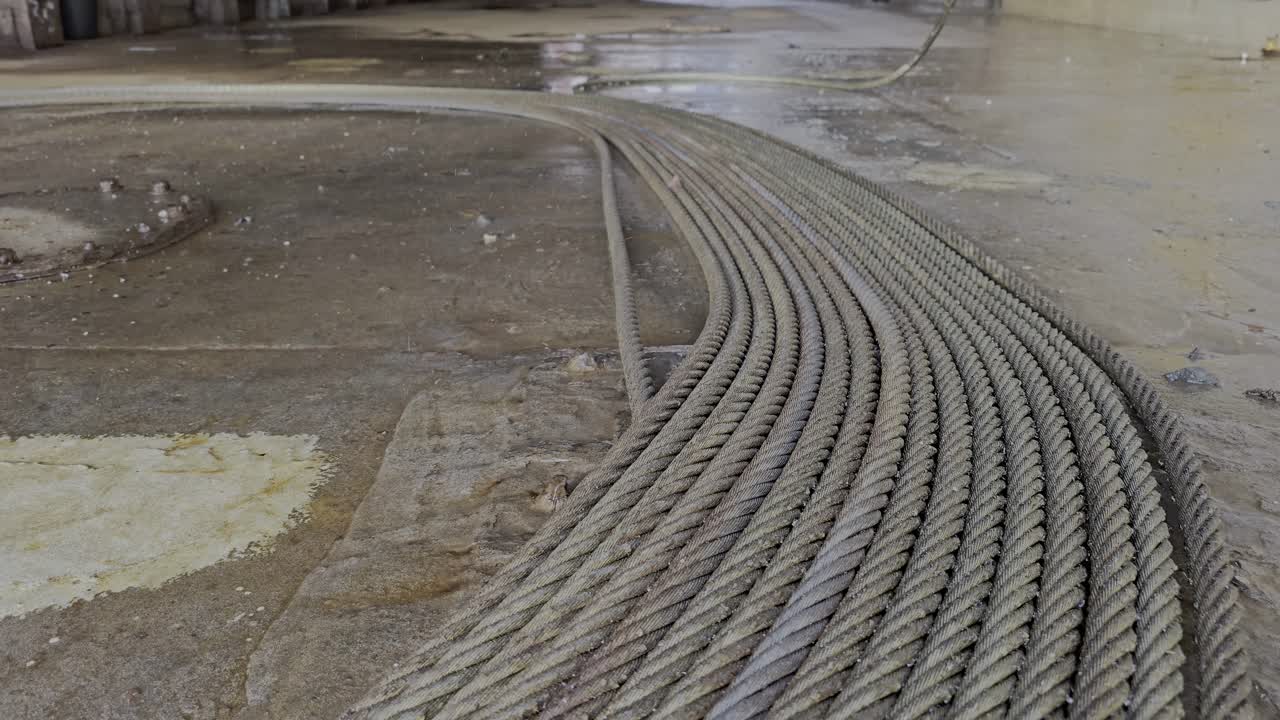 Heavy steel wire lies coiled on wet ground as water drips nearby. Suggests wear, use, and inspection