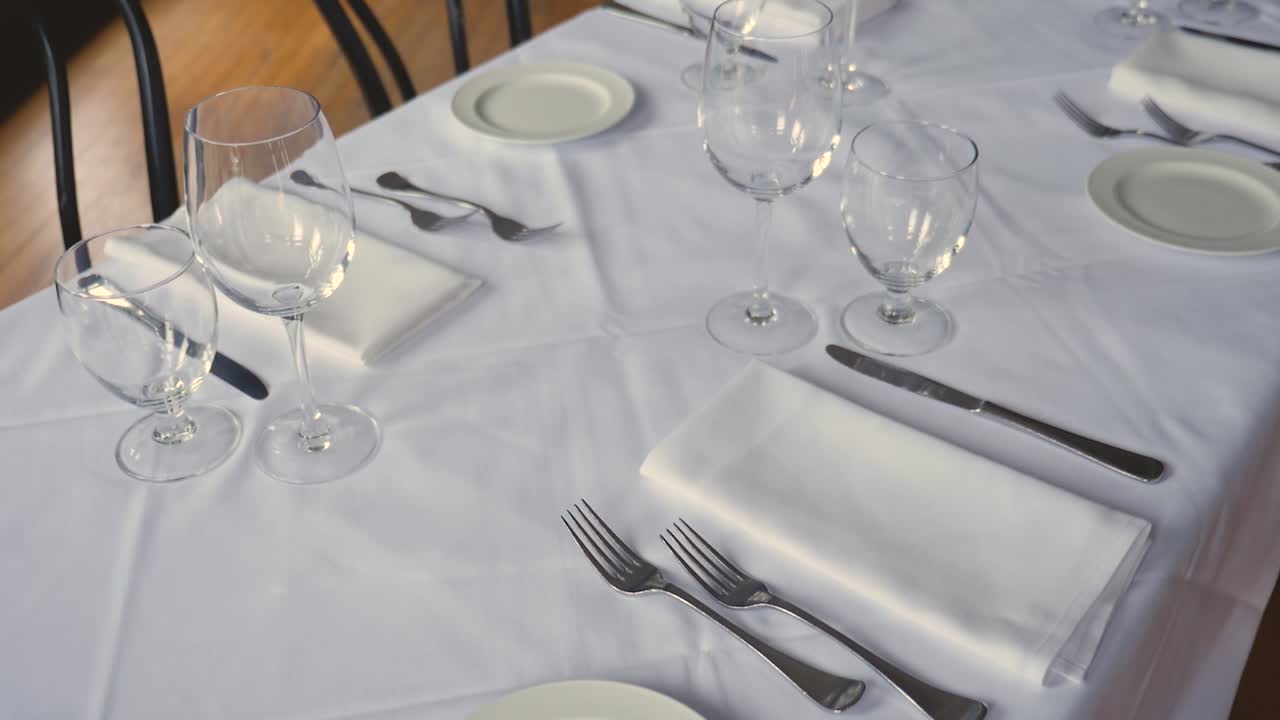 mesa de comedor para una boda o evento corporativo en un restaurante de alta cocina platos de cerámica tenedores cuchillos servilletas de tela sobre un mantel blanco en la mesa constante cámara lenta de ancho medio panorámico hacia arriba