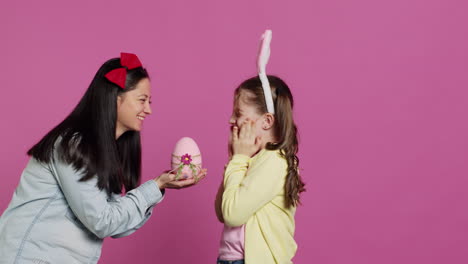 lovely mother surprising her daughter with a cute pink egg for easter