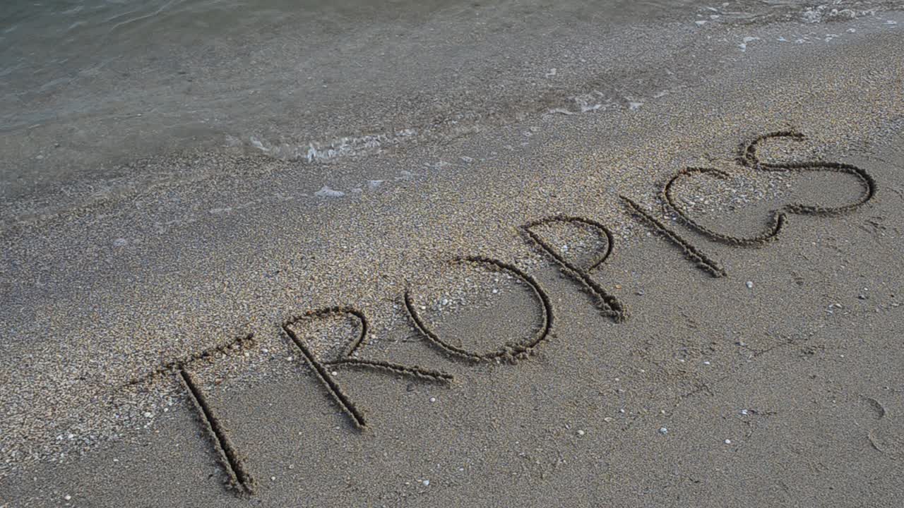 Inscription Tropics in the sand. Shooting on the beach