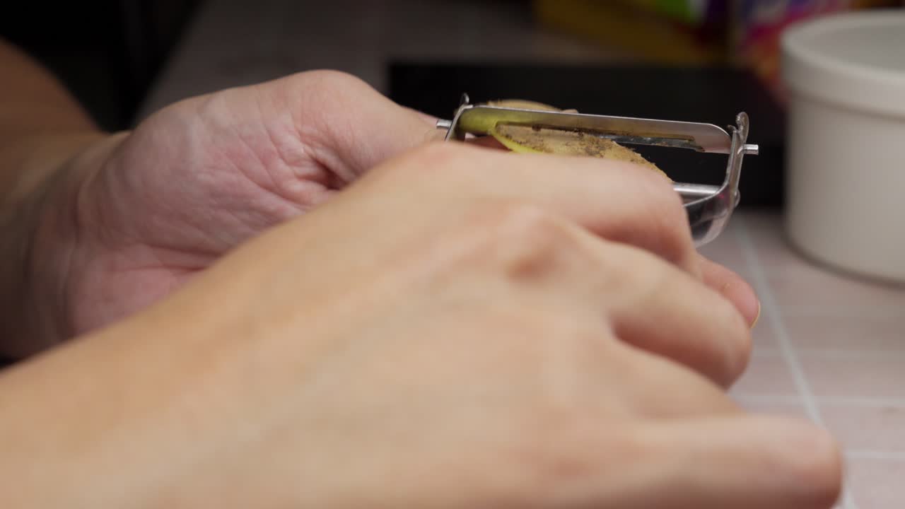 Uomo che pela una patata con un pelapatate in cucina. Primo piano