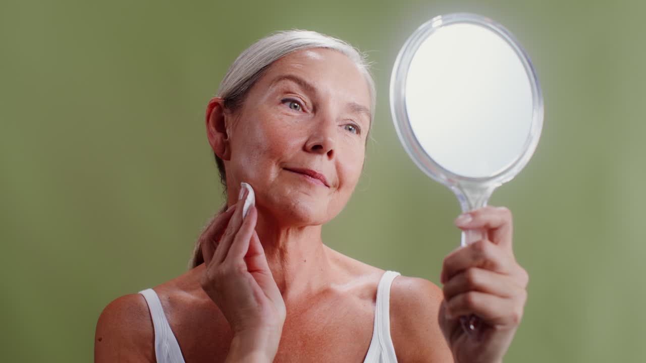 Mature woman looking in the mirror and cleaning her face