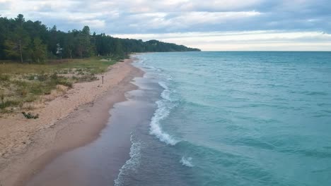aerial tilt down view of ocean blue waves break on a beach. sea waves and beautiful sand beach aerial view drone shot. hoeft state park in michigan.