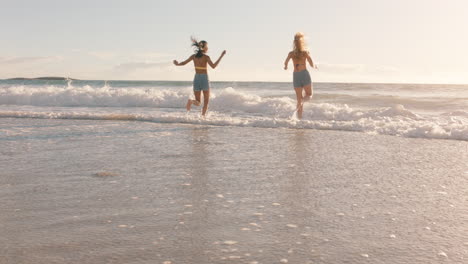 teenage girls running on beach into sea splashing in water having fun best friends enjoying warm summer day on vacation