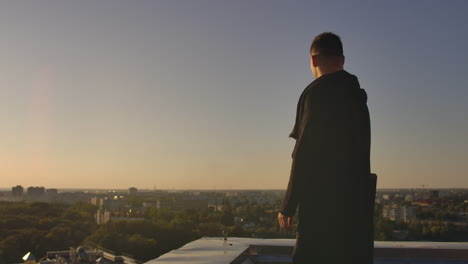 hacker using laptop on rooftop with city view and forex chart. hacking and stats concept. a man at sunset in slow motion writing software code on a laptop