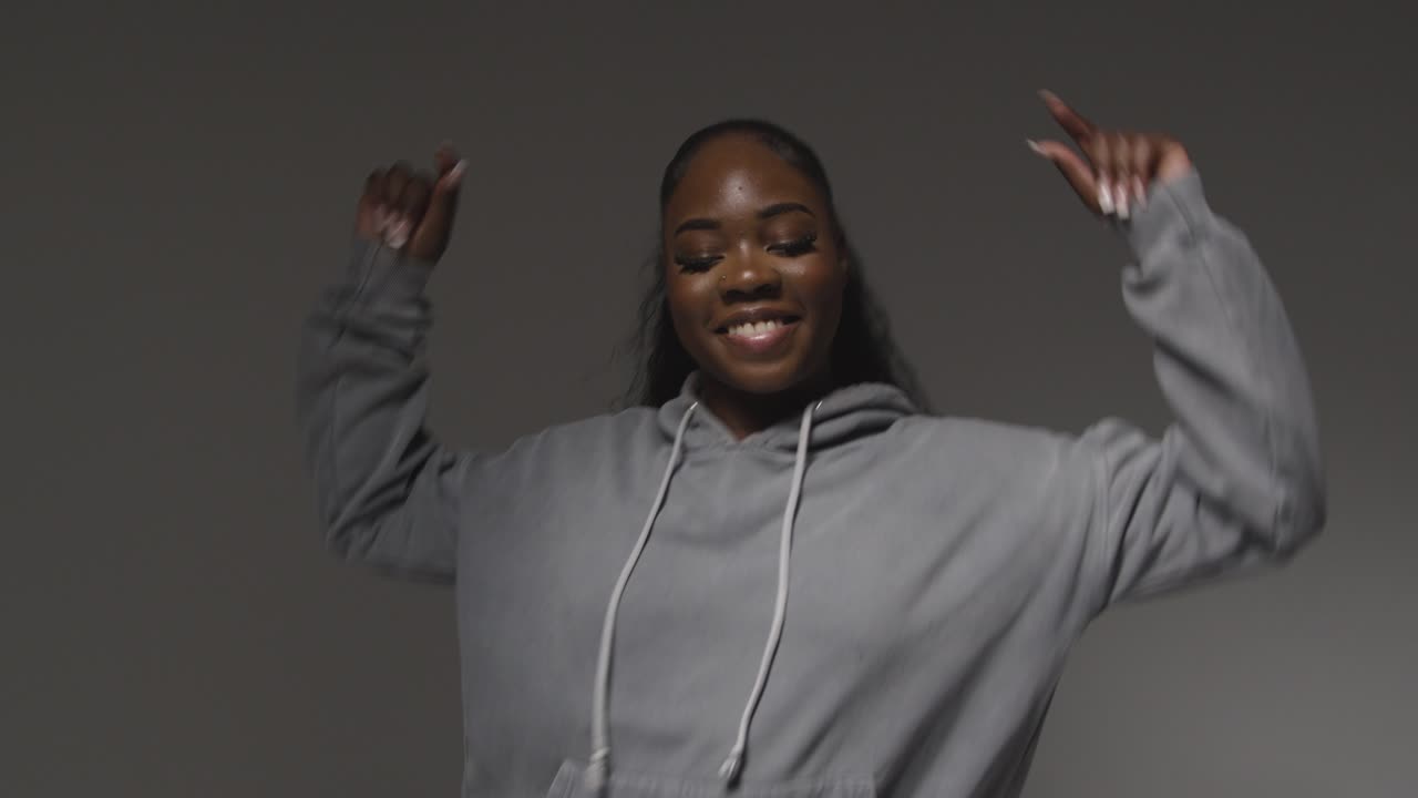 Studio Portrait Shot Of Young Woman Wearing Hoodie Dancing With Low Key Lighting Against Grey Background 3