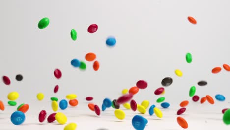 bright colored chocolate m and m candies bouncing, dancing and spinning on white table top in slow motion