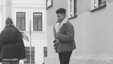 black and white view of a sax case on the floor and a man in jacket playing sax in the street