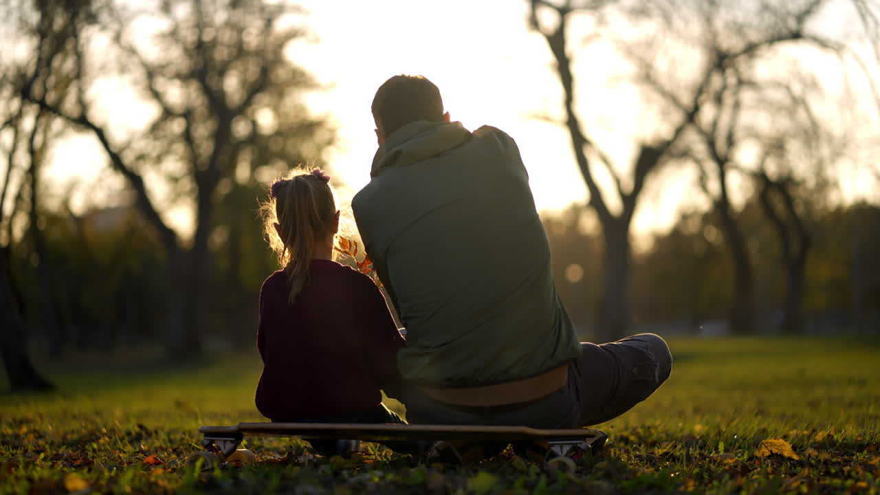 Father and daughter enjoying sunset in the park on a skateboard