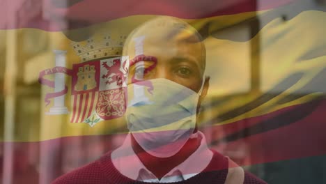 animation of flag of spain waving over man wearing face mask during covid 19 pandemic