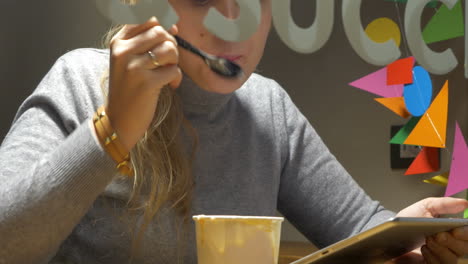 woman in cafe eating ice-cream and using pad