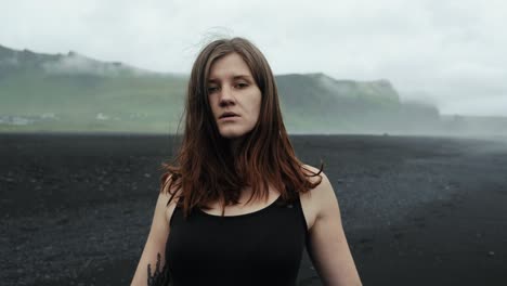 young beautiful woman in black dress dancing on black sand beach iceland, slow motion looking into camera, dramatic waves seascape