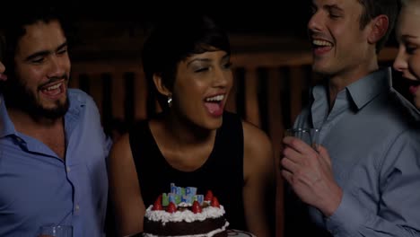 Group-of-smiling-friends-blowing-candle-while-celebrating-birthday-in-bar