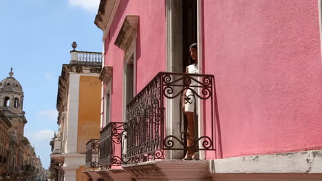 woman on balcony of pink building