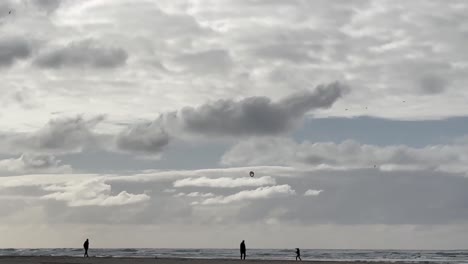 family silhouette at beach with kid flying kite on sunny day. wide shot