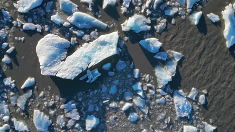 scattered chunks of calved iceberg floating in glacier lake, aerial top down